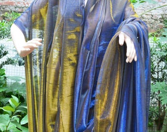 May include: A shimmering, sheer shawl in shades of blue and gold. The fabric drapes over a mannequin, showcasing its flowing design. The color transitions create a dynamic visual effect, suitable for evening wear or special occasions.
