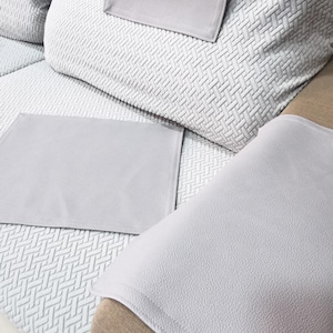 May include: A light grey sofa with a textured, geometric pattern on the cushions and armrests. The sofa has matching light grey armrest covers. The cushions are rectangular and square.