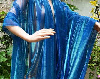 May include: A flowing, sheer blue garment with long sleeves and a draped neckline. The fabric has a shimmering, iridescent quality, catching the light and creating a dynamic visual effect. The garment appears to be lightweight and suitable for layering or as a cover-up.
