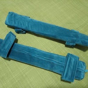 Puede incluir: Dos almohadas de tela azul con correas y cremalleras. Las almohadas son rectangulares y tienen una textura suave y mullida.