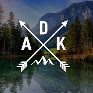 May include: A white logo with the letters "DAK" in a bold font, with two arrows crossing each other. The arrows point to the left and right. The logo is set against a background of a lake and mountains.