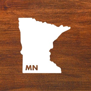 May include: White outline of the state of Minnesota on a brown wooden background. The state abbreviation "MN" is written in white inside the outline.