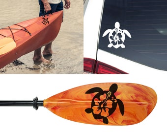 May include: A black and white silhouette of a turtle with a hibiscus flower on its back. The design is on a wooden paddle, a kayak, and a car window.