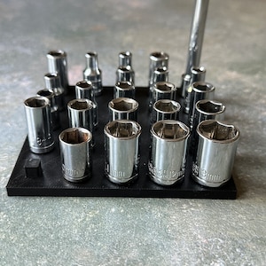 Könnte beinhalten: Ein schwarzer Sockel-Organizer aus Kunststoff mit einer Vielzahl von verchromten Sockeln in verschiedenen Größen. Die Sockel sind in Reihen und Spalten auf dem Organizer angeordnet. Der Organizer hat einen kleinen schwarzen Kunststoffständer auf der Unterseite.