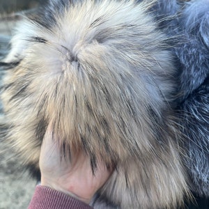 May include: A fluffy, grey and white fur pom pom. The pom pom is made of real fur and has a soft, luxurious feel.