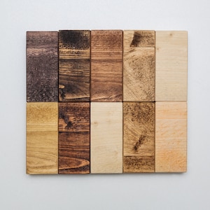 以下が含まれることがあります： 茶色、ベージュ、薄い茶色の様々な色合いの木製のブロック12個のセット。ブロックはグリッドパターンに配置されています。