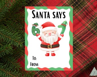 Puede incluir: Una etiqueta de regalo con temática navideña con un Papá Noel de dibujos animados sosteniendo los números 6 y 7. La etiqueta tiene un borde rojo y verde y las palabras "SANTA SAYS" en la parte superior. Espacio para escribir "Para:" y "De:"
