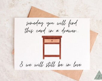 Puede incluir: Una tarjeta blanca con texto escrito a mano en negro que dice "someday you will find this card in a drawer... & we will still be in love". La tarjeta presenta una ilustración simple de una mesita de noche de madera marrón con un cajón.