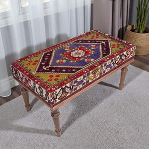 Pode incluir: Banqueta retangular com um tampo estampado colorido. O design apresenta uma forma de diamante azul central com detalhes em vermelho, verde e amarelo. As pernas de madeira são de cor castanho claro. A banqueta tem cerca de 120 cm de comprimento.
