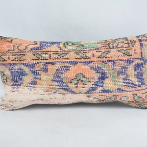 May include: A rectangular pillow with a colorful, patterned design. The pillow is made of a woven fabric with a peach, blue, green, and black pattern.