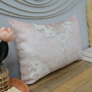 May include: A pink and white patterned throw pillow with a subtle floral design. The pillow is made of a soft, woven fabric and has a relaxed, bohemian style.