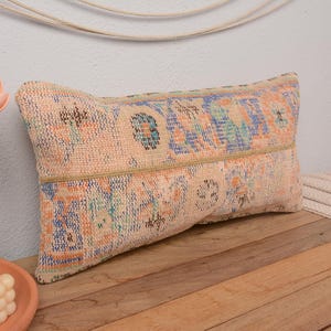 May include: A long, rectangular cushion with a colourful, floral pattern. The cushion is made of a soft, woven fabric and has a beige background with blue, green, and orange accents.