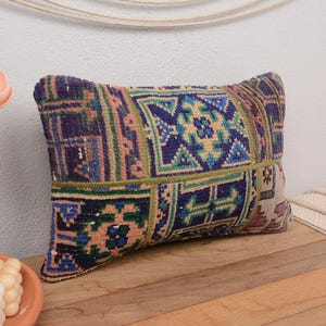 May include: A colorful, patterned pillow with a patchwork design in shades of blue, green, and beige. The pillow is made of woven fabric and has a rectangular shape.