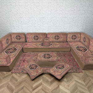 Könnte beinhalten: Ein großes Ecksofa in U-Form mit passendem Teppich und Kissen. Das Sofa und der Teppich weisen ein sich wiederholendes geometrisches Muster in Rosa, Braun und Schwarz auf.