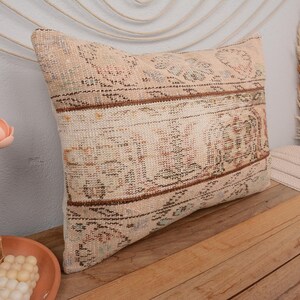 Könnte beinhalten: Ein beige-braunes, gemustertes Kissen mit einem verblassten, Vintage-Look. Das Kissen ist aus gewebtem Stoff und hat ein dezentes Blumenmuster.