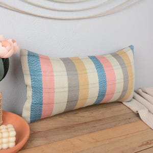 May include: A striped throw pillow with blue, pink, yellow, and gray stripes. The pillow is on a wooden surface.