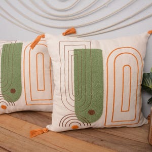 May include: Two decorative throw pillows with orange tassels. The pillows are white with orange and green geometric designs.