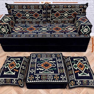 May include: A dark blue sofa set with a geometric pattern in orange, green, and white. The set includes a sofa, two armrests, and three floor cushions. The sofa is 190 cm wide and 40 cm high.
