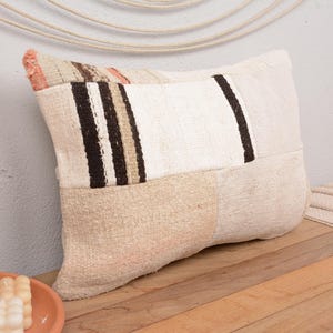 Könnte beinhalten: Ein weißes und beigefarbenes Patchwork-Kissen mit braunen Streifen. Das Kissen ist aus einem weichen, gewebten Stoff gefertigt und hat eine leicht strukturierte Oberfläche.