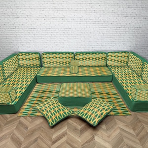 Può includere: Un set di divani componibili verdi con un motivo geometrico giallo e verde. Il set comprende un divano grande, un tappeto, due cuscini e un piccolo pouf. L'arredamento è disposto su un pavimento in legno.