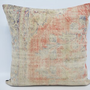 May include: A square throw pillow with a faded, vintage-style pattern in shades of blue, red, and cream. The pillow has a subtle, distressed look and a woven texture.