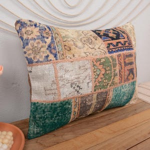 May include: A patchwork pillow cover with a variety of colors and patterns, including beige, brown, green, blue, and white. The pillow cover is made of a soft, woven fabric and has a fringed edge.