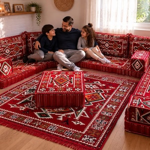 May include: A red floor seating set featuring a modular sofa with backrests and a matching square ottoman. The cushions and rug display a geometric pattern in red, white, black, and green. The set includes floor cushions and armrests.