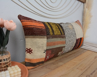 May include: A long, rectangular pillow with a patchwork design. The pillow is made of various fabrics in shades of brown, orange, beige, and gray. The pillow is lying on a wooden surface.