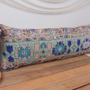 Peut inclure: Un long coussin rectangulaire avec un motif de tapis vintage. Le coussin présente un motif floral turquoise, bleu et rose. Le coussin est posé sur une surface en bois.