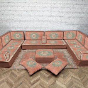 May include: A U-shaped modular sofa in coral fabric, patterned with green and white. Includes a matching rug, ottoman, and two cushions. The sofa sits on a wooden floor. Measurements are in cm.