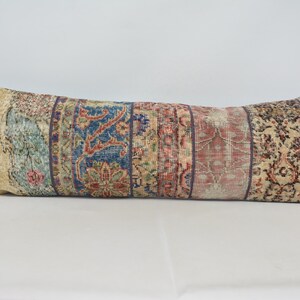 May include: A long, rectangular pillow with a colorful, patterned fabric. The fabric is made up of several different strips of fabric, each with a different pattern. The colors in the fabric include beige, red, blue, and green.