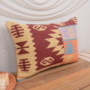 May include: A decorative throw pillow with a geometric pattern in shades of yellow, red, orange, blue, and purple. The pillow is made of woven fabric and has a fringed edge.