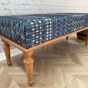 May include: A wooden bench with turned legs and a blue and white patterned fabric seat.
