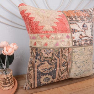 May include: A patchwork pillow with a geometric design in shades of red, orange, and beige. The pillow has a vintage, distressed look, with visible stitching and varied textures. The pillow is square and appears to be made of woven fabric.