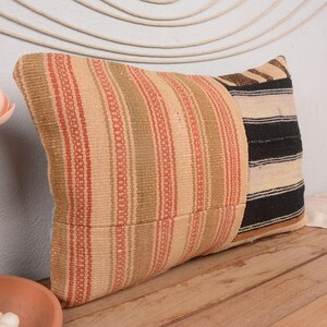 Puede incluir: Dos cojines decorativos. Uno presenta rayas verticales en beige, rojo y marrón. El otro tiene rayas horizontales negras y beige. Los cojines están hechos de tela tejida.