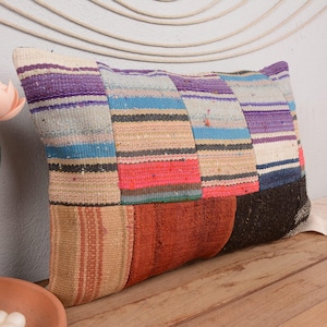 May include: Rectangular decorative pillow with a patchwork design. The pillow features a mix of colors including purple, blue, red, and brown. The pillow is placed on a wooden surface.