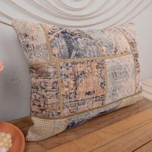 Puede incluir: Una almohada rectangular de patchwork con un patrón beige, marrón y azul. La almohada está hecha de una tela suave y tejida con un brillo sutil.