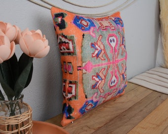 May include: A decorative pillow with a colorful geometric pattern in shades of orange, pink, blue, and green. The pillow is made of a soft, woven fabric and has a fringed edge.