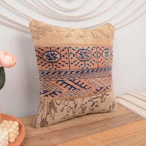 May include: A decorative throw pillow with a beige background and a colorful geometric pattern in shades of blue, orange, and pink. The pillow is made from a woven fabric and has a fringed edge.