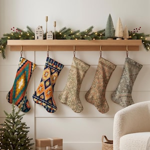 Könnte beinhalten: Fünf Weihnachtsstrümpfe hängen an einem Kaminsims aus Holz. Der erste zeigt ein lebhaftes geometrisches Muster in Orange, Blaugrün und Gelb. Der zweite hat ein blaues Rautenmuster. Die restlichen drei zeigen dezente, komplexe Vintage-Muster.