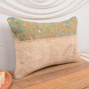 May include: A rectangular pillow with a beige and green patterned fabric. The pillow has a light beige color with a green and blue patterned band across the top.