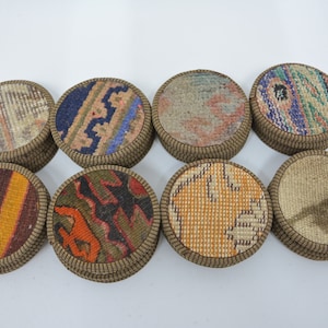 May include: Eight round fabric coasters with different patterns. The coasters are made of a woven fabric with a brown border. The patterns include stripes, geometric shapes, and floral designs.