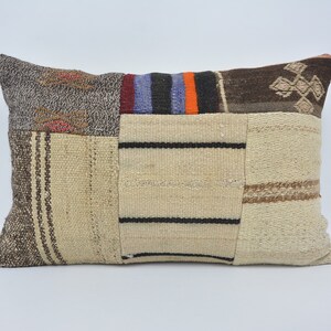 May include: A rectangular patchwork pillow with a beige background and brown, black, orange, and blue stripes. The pillow is made of woven fabric and has a variety of textures.