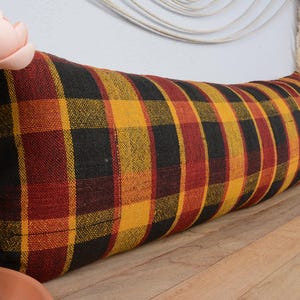 May include: A long, rectangular pillow with a black, red, and yellow plaid pattern. The pillow is made of a woven fabric and has a soft, comfortable texture.