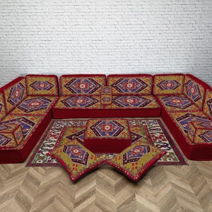 May include: A red sectional sofa with patterned cushions and a matching rug. The cushions feature a geometric design in shades of blue, yellow, and red. The sofa is arranged in a U-shape.