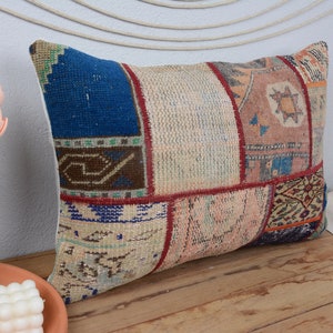 May include: A patchwork pillow cover featuring a mix of colours and patterns, including blue, red, brown, and beige. The pillow cover is crafted from woven fabric and has a fringed edge.