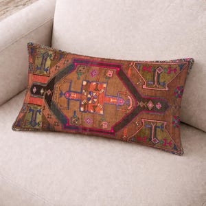 Könnte beinhalten: Rechteckiges Zierkissen mit einem geometrischen Muster in Braun, Rot und Blau. Das Kissen hat ein detailliertes Design mit verschiedenen Formen und Farben, darunter Orange, Rosa und Grün. Das Kissen liegt auf einem hellen Sofa.