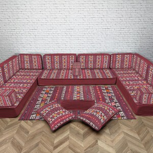 May include: A red sectional sofa set with a matching rug and two cushions. The furniture features a patterned design in red, orange, and white. The rug and cushions have a similar pattern, creating a cohesive look.