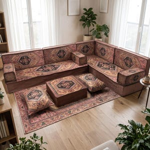 May include: A modular floor sofa set featuring a multi-piece sectional with backrests and armrests, a square ottoman, and two rectangular floor cushions. All pieces are upholstered in a fabric with a repeating geometric pattern in pink, brown, and black.