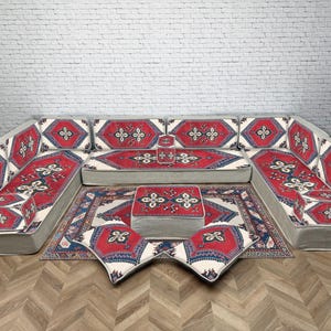 May include: A U-shaped sectional sofa with a matching rug and ottoman. The set has a red, white, and blue geometric pattern on a grey base. The sofa has multiple cushions and is designed for comfort.